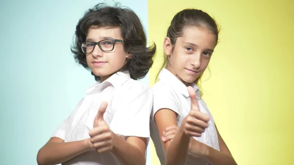 Çocuklar okulda bir renkli arka plan üzerinde üniforma portreleri. Komik çocuk. Kız ve erkek kardeş. Okul kavramı. Kameraya bak ve başparmak sırıtmak. kopya alanı — Stok fotoğraf