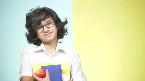 Portretten van een tiener jongen op school uniform op een gekleurde achtergrond. Grappige kerel. concept van leren. Een tiener houdt boeken kijken naar de camera en glimlachen. kopie ruimte — Stockfoto