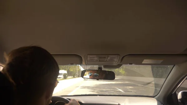 Un jeune bel homme en lunettes de soleil conduit une voiture à grande vitesse, le long d'une autoroute avec vue sur les montagnes . — Photo