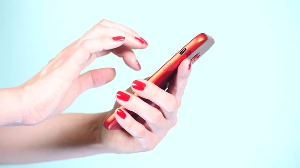 Närbild, kvinnlig händer med rött manikyr använder en smartphone på en färgad bakgrund. — Stockfoto