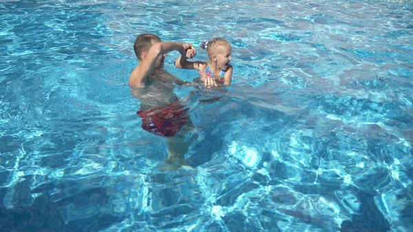 Mladý otec učí svou malou dceru plavat v bazénu. Šťastná dívka a její otec se smát a bavit se. — Stock fotografie