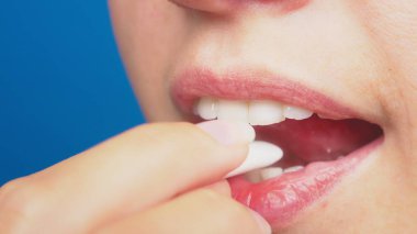 yakın çekim, Bayan dudak makyaj olmadan kız ağzına sakız koyar. mavi bir arka plan üzerinde