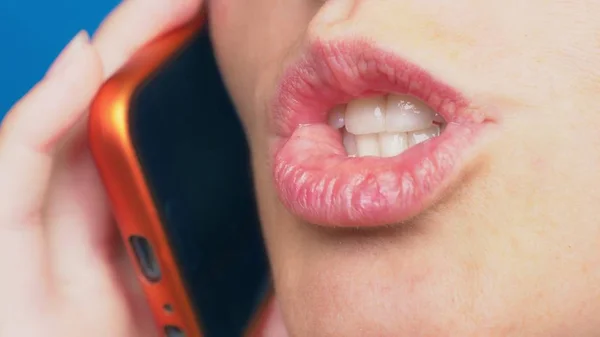 Primer plano, labios femeninos sin maquillaje hablando en un teléfono móvil rojo, sobre un fondo azul . —  Fotos de Stock