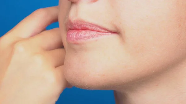 Primer plano, labios de mujer sin maquillaje, la chica toca su cara con su mano. sobre un fondo azul — Foto de Stock