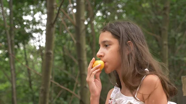 かわいい女の子ブルネット、果物を食べると話しています。自然の背景. — ストック写真