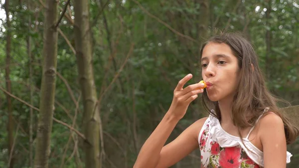 Χαριτωμένο μικρό κορίτσι μελαχρινή, τρώγοντας φρούτα και μιλάμε. Φύση φόντο. — Φωτογραφία Αρχείου
