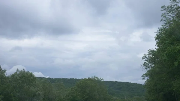 Blick aus dem Autofenster auf eine bergige Landschaft, Kumuluswolken und Bäume an einem bewölkten Sommertag. — Stockfoto