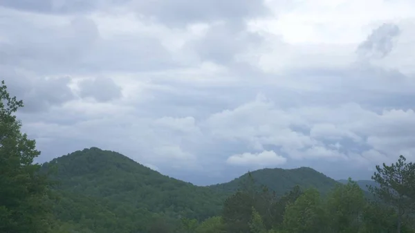 Blick aus dem Autofenster auf eine bergige Landschaft, Kumuluswolken und Bäume an einem bewölkten Sommertag. — Stockfoto