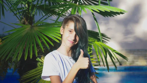 Hermosa chica morena posando sobre un fondo de hojas de palma. Una adolescente con el pelo rizado largo azul. verano día soleado . —  Fotos de Stock