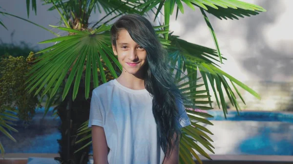 Όμορφη μελαχρινή κοπέλα ποζάρει σε φόντο της παλάμης φύλλα. Έναν έφηβο κορίτσι με μπλε μακριά σγουρά μαλλιά. ηλιόλουστη μέρα του καλοκαιριού. — Φωτογραφία Αρχείου