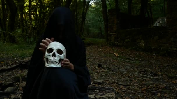 Verschrikkelijke boze heks in de herfst bos houdt een menselijke schedel, zittend op een logboek. — Stockvideo