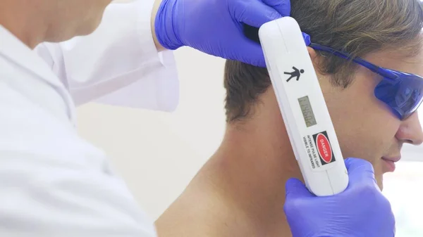 Depilación láser para hombre. el médico con guantes azules quita el pelo de los hombros y el cuello de un joven guapo. primer plano . — Foto de Stock