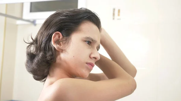 Carino ragazzo spazzolatura la sua ricci capelli di fronte il bagno specchio . — Foto Stock