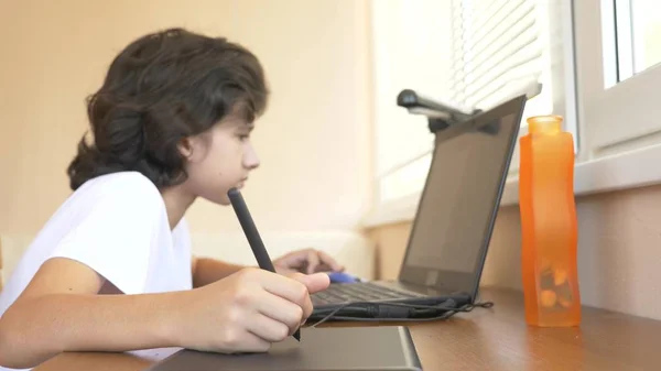 Vacker modern pojke tonåring arbetar med en ritplatta. Han ser på den bärbara skärmen. — Stockfoto