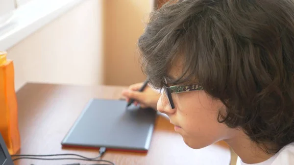 Przystojny chłopak nowoczesne nastolatek działa na tablecie graficznym. patrzy na ekranie laptopa. — Zdjęcie stockowe