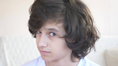 kıvırcık saçlı yakışıklı genç kamera gülüyor içine bakar ve komik bir yüz ifadesi yapar.