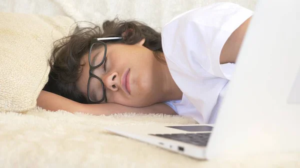 Nastolatek ładny chłopak w okularach śpi na kanapie obok laptopa. — Zdjęcie stockowe
