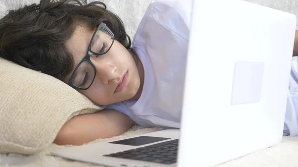 Söt pojke tonåringen bär glasögon sover på soffan bredvid laptop. — Stockfoto
