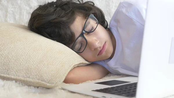 Söt pojke tonåringen bär glasögon sover på soffan bredvid laptop. — Stockfoto