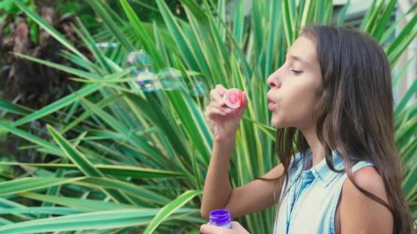 Menina adolescente morena soprando bolhas de sabão contra um parque tropical fundo . — Fotografia de Stock