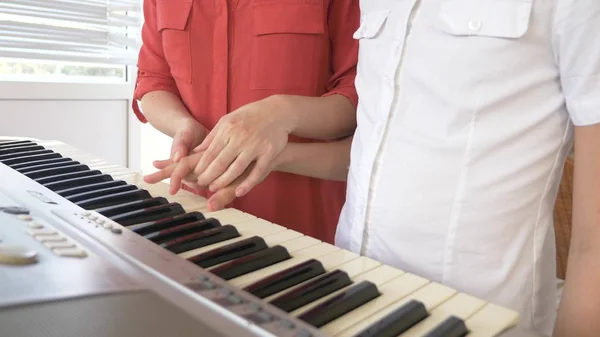 Primo piano. un insegnante di pianoforte insegna a un bambino a suonare il pianoforte, mettendo le mani . — Foto Stock