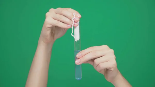 Primer plano, las manos femeninas colocan el hisopo en un tubo de ensayo con líquido azul, para comprobar la fuerza del tampón. sobre un fondo verde . —  Fotos de Stock