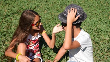 Erkek ve kız, 10-12 yaşında ikiz güneşli bir yaz parkta bir açıklıkta oturuyor. sevinirler ve kucaklamak.