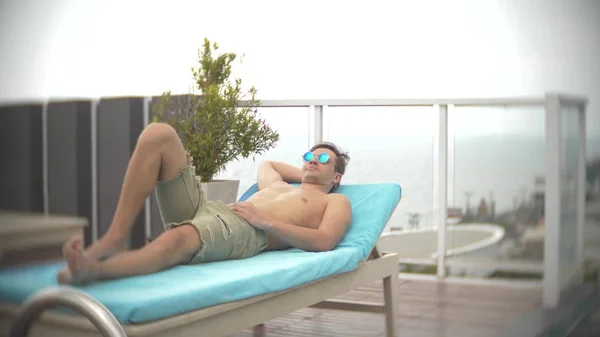 Ein Mann, der sich auf den Liegestühlen in der Nähe des Pools auf dem Dach mit Blick auf das Meer entspannt. Hintergrundunschärfe — Stockfoto
