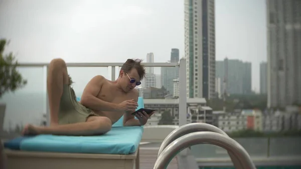 젊은 남자는 바다가 내려다 보이는 지붕에 수영장에서 태블릿 배경 흐림 — 스톡 사진