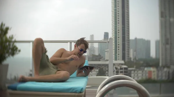 Deniz manzaralı çatı havuzunda bir tablet ile genç bir adam arka plan bulanıklık — Stok fotoğraf