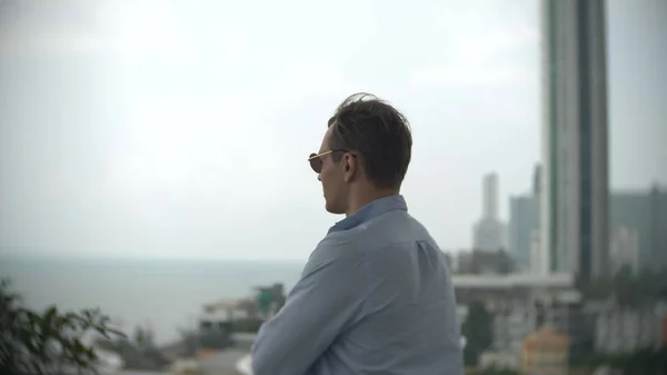 a man looking into the distance, standing on the terrace overlooking the sea, background blur