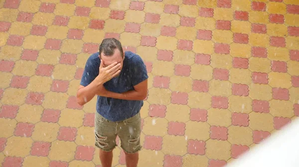 Ein junger gutaussehender Kerl freut sich im Regen, indem er die Hände hebt und Regenwasser wäscht — Stockfoto