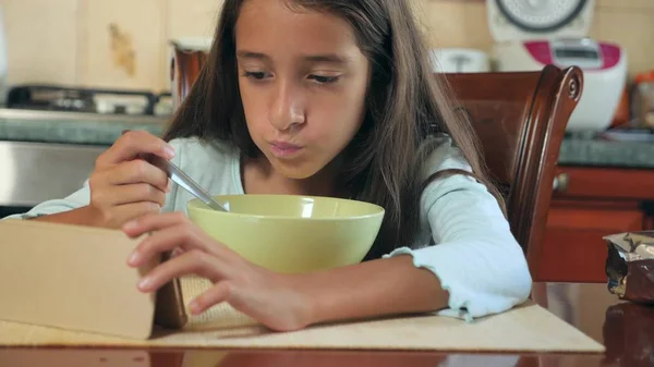 8-10 세 소녀 부엌 테이블에 우유와 함께 아침 시리얼을 먹는다 고 그녀의 스마트폰으로 본다. — 스톡 사진