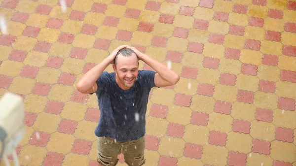 Ein junger gutaussehender Kerl freut sich im Regen, indem er die Hände hebt und Regenwasser wäscht — Stockfoto