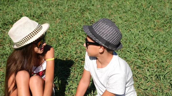 Chłopiec i dziewczynka, bliźniaki 10-12 lat siedzą na Polanie w parku w słoneczny letni dzień. Radujcie się i ogarnąć. — Zdjęcie stockowe