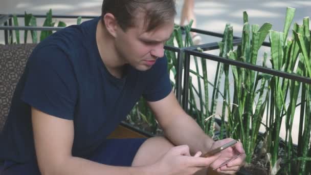 Un hombre utiliza su tarjeta bancaria y teléfono mientras está sentado en un café de un gran complejo comercial — Vídeos de Stock