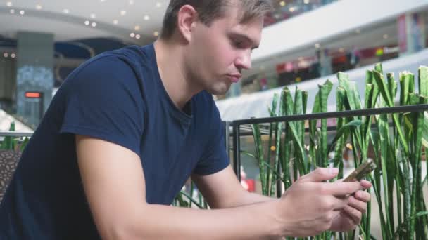 Een man maakt gebruik van zijn bankkaart en telefoon zittend in een café een grote shopping complex — Stockvideo