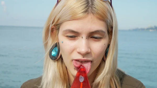 Close-up portrait of a young blonde girl with a splitted tongue, she licks a lollipop. copy space — Stock Photo, Image