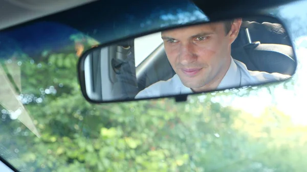 Мужчина-бизнесмен в рубашке и галстуке водит машину и просматривает сообщение на телефоне. нарушение правил дорожного движения. вид в зеркало заднего вида — стоковое фото