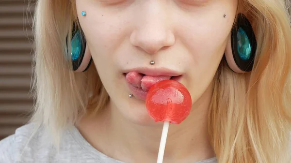 Close-up portrait of a young blonde girl with a splitted tongue, she licks a lollipop. copy space — Stock Photo, Image