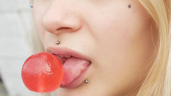 Close-up portrait of a young blonde girl with a splitted tongue, she licks a lollipop. copy space — Stock Photo, Image