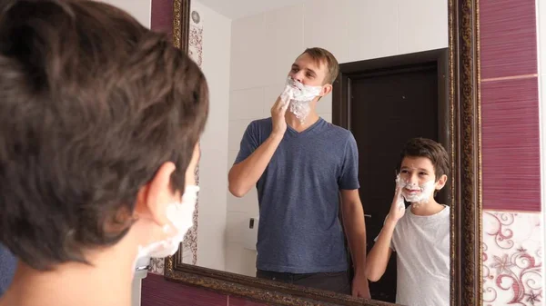 Father and son in the bathroom in the morning, little boy copies his father shaving. — Stock Photo, Image