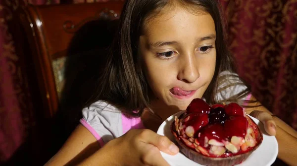 A little girl is happy to eat a chocolate cake with fresh berries. she licks — Stock Photo, Image