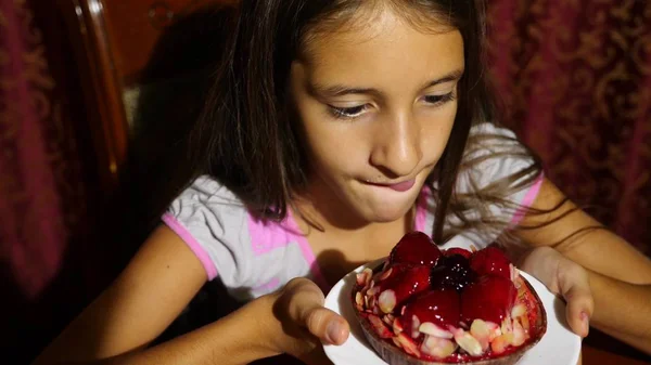 Uma menina está feliz em comer um bolo de chocolate com bagas frescas. ela lambe — Fotografia de Stock