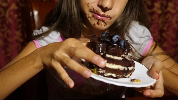 Seorang gadis kecil makan kue dengan buah berry segar. wajahnya dalam coklat, dia bahagia — Stok Foto