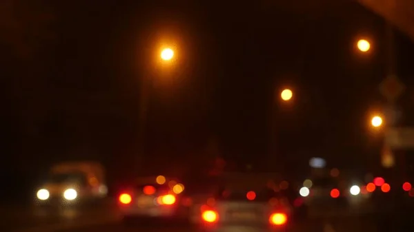 Conduzir à noite. carros desfocados na cidade. Janela de carro frontal iluminada com trânsito turvo da cidade nas ruas da cidade . — Fotografia de Stock