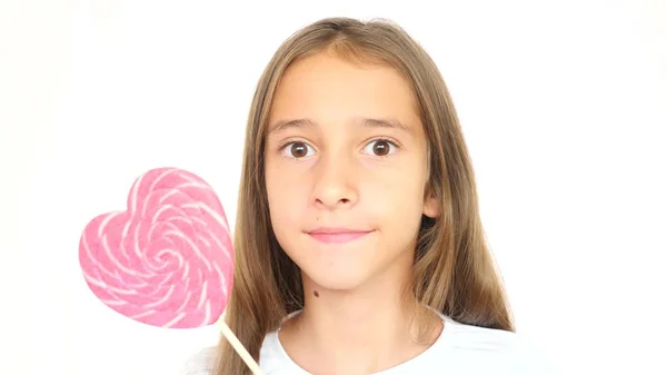 Niña lamiendo una piruleta en forma de un gran corazón rosa. espacio de copia — Foto de Stock