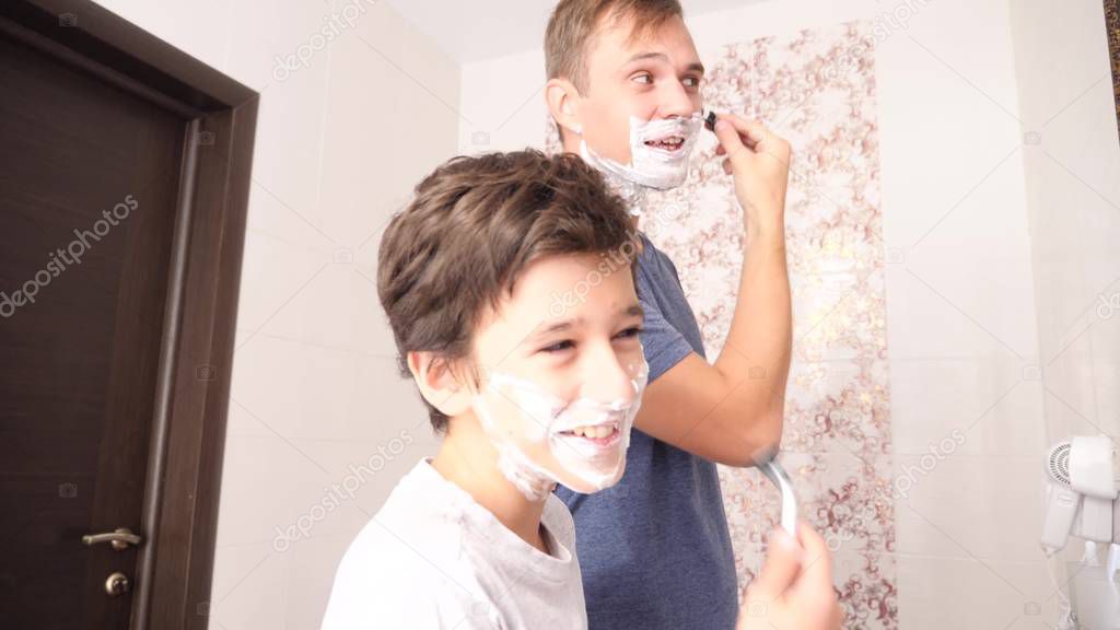Father and son in the bathroom in the morning, little boy copies his father shaving.