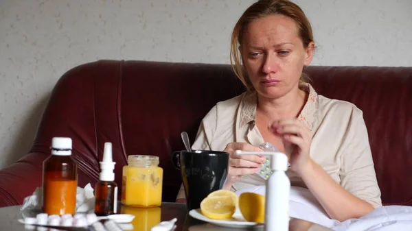 De leugens van de zieke vrouw op de Bank in haar woonkamer, op de tafel naast haar er zijn medicijnen en een warme drank met honing en citroen. — Stockfoto