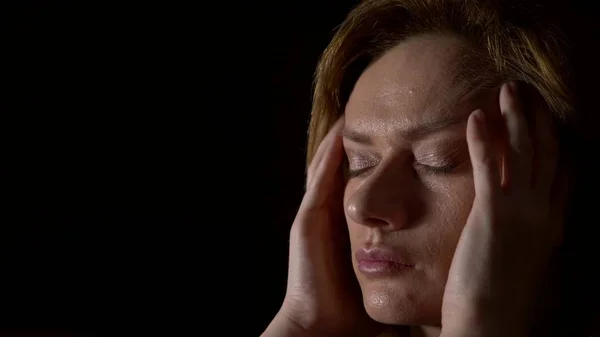 Nahaufnahme, traurige Frau mit Kopfschmerzen auf dunklem Hintergrund. — Stockfoto